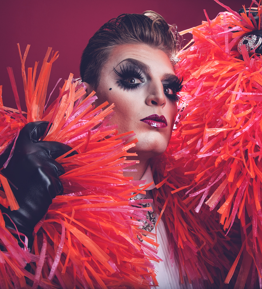 Thumbnail image. Person with extravagant makeup and fringed coat looking into the camera dramatically.  