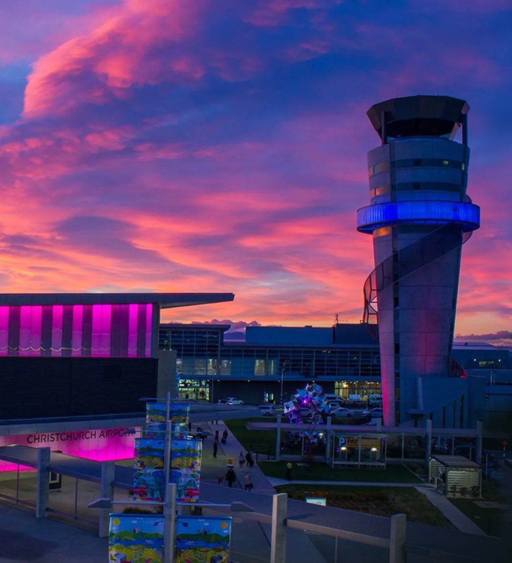 Thumbnail image. Christchurch Airport at sunset, with a glowing control tower, magenta-lit terminal, and vibrant sky.