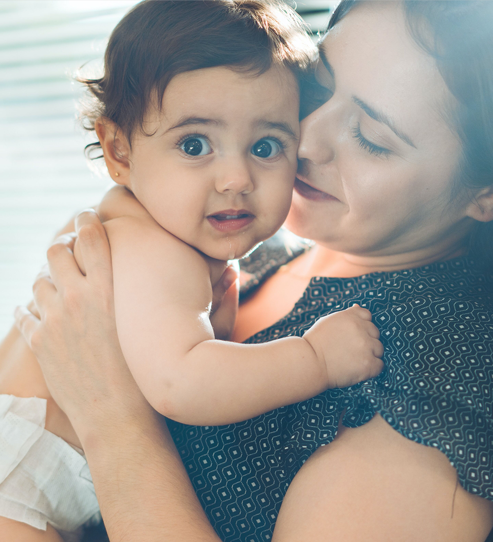 Thumbnail image. A mother holding her baby close to her chest. The baby is looking directly at the camera.