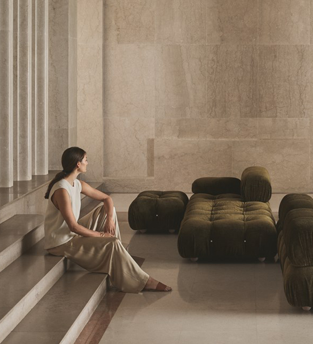 Thumbnail image. A luxurious home interior featuring a woman sitting on steps in-front of a olive green Matisse sofa.
