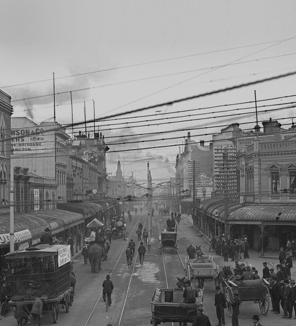 Thumbnail Image.Hero image. A historic photo of High Street, Christchurch, NZ, showing a busy scene with pedestrians, horse-drawn carriages, cyclists, and tram cables overhead.