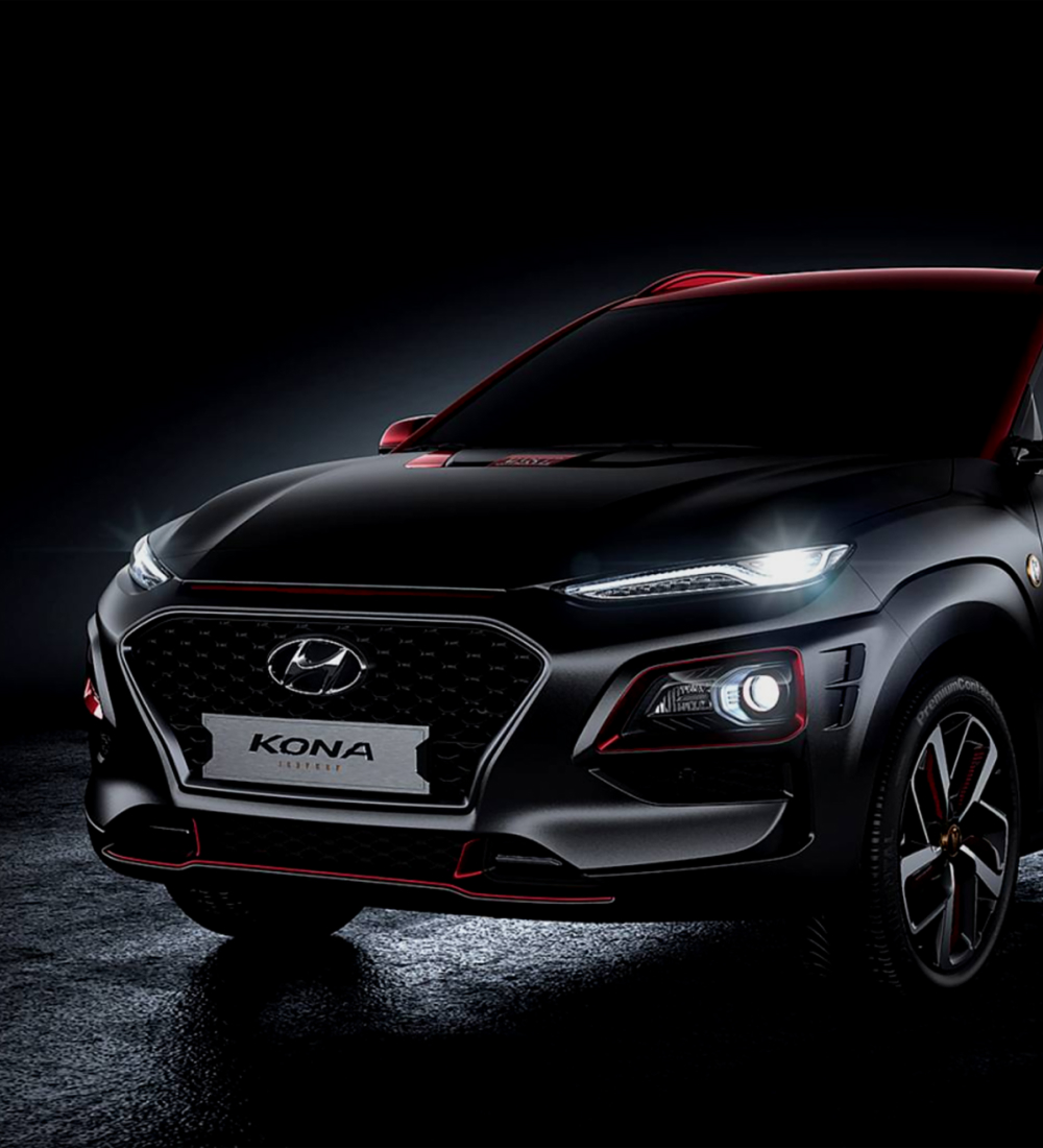 Thumbnail image. The front of a sleek Hyundai Kona with bold red accents, illuminated in a dark setting
